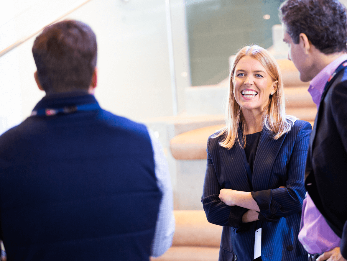 Woman wearing suit with arms crossed smiling at two men in professional setting.